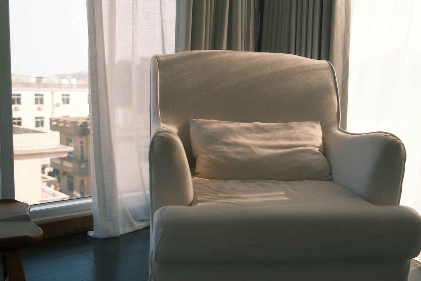 A white armchair with a pillow by the window.